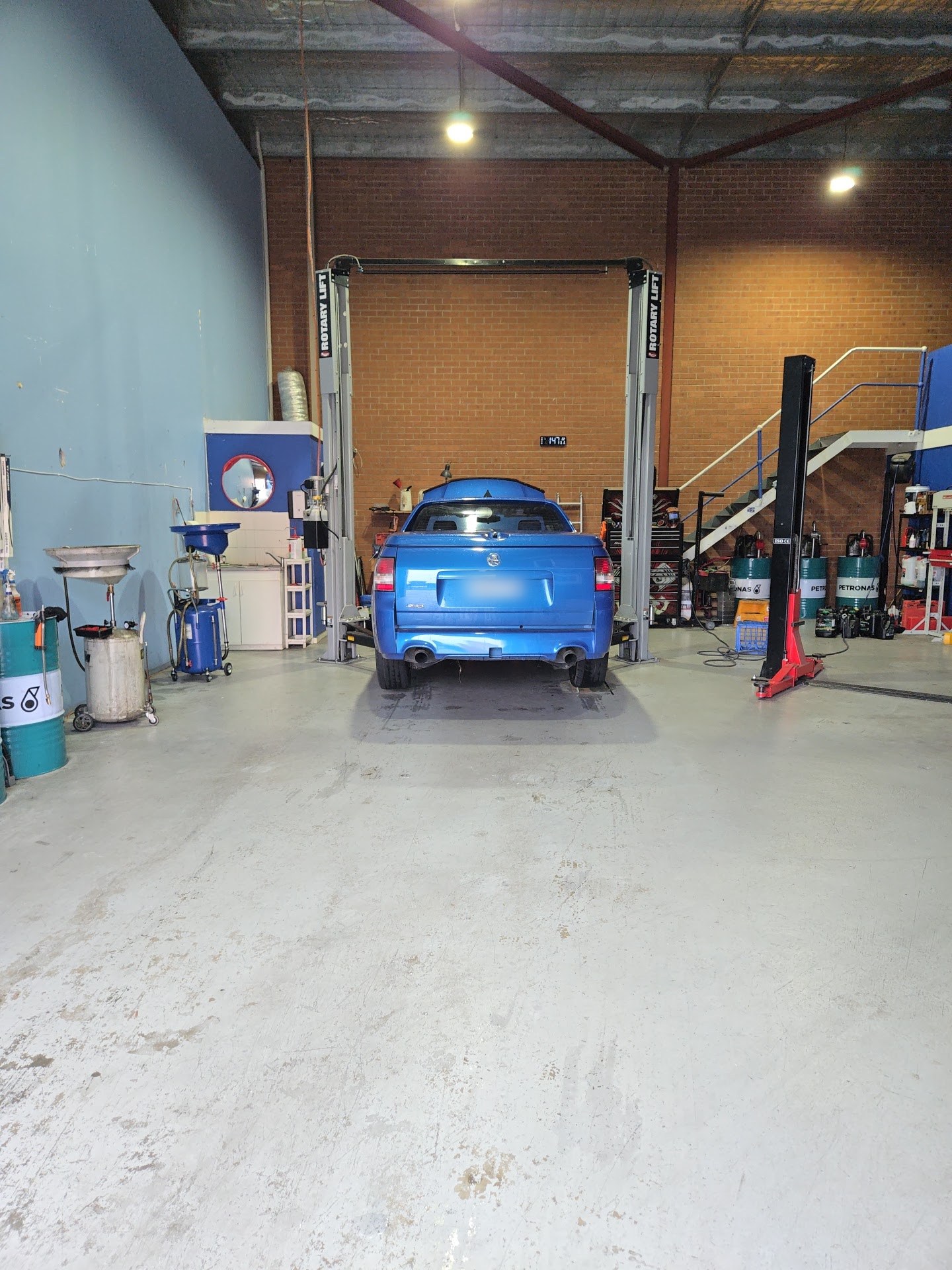 A blue ute in the service bay at KR Auto Repair, with the oil drainer and drums alongside